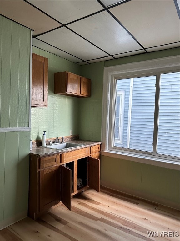 bar featuring a paneled ceiling, a sink, and light wood finished floors