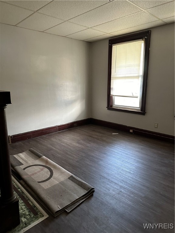 empty room with a paneled ceiling, baseboards, and wood finished floors