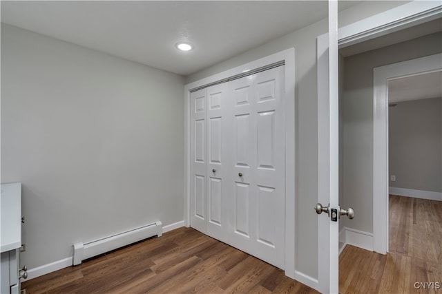 unfurnished bedroom with hardwood / wood-style floors, a closet, and baseboard heating