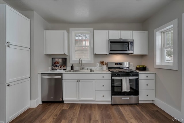 kitchen with a sink, white cabinets, light countertops, appliances with stainless steel finishes, and dark wood-style floors