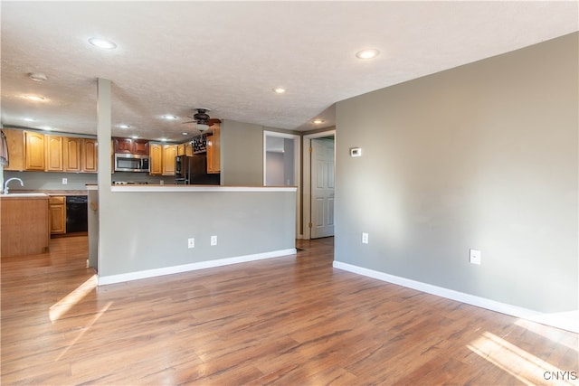 kitchen featuring sink, kitchen peninsula, a textured ceiling, black appliances, and light wood-type flooring