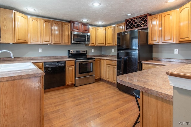 kitchen with a breakfast bar, black appliances, sink, light hardwood / wood-style flooring, and kitchen peninsula