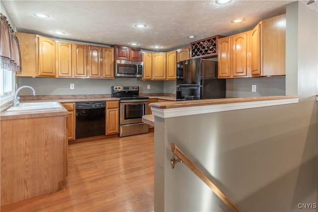 kitchen with black appliances, sink, light wood-type flooring, a textured ceiling, and kitchen peninsula