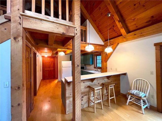 kitchen featuring pendant lighting, a breakfast bar, white refrigerator, light hardwood / wood-style flooring, and kitchen peninsula