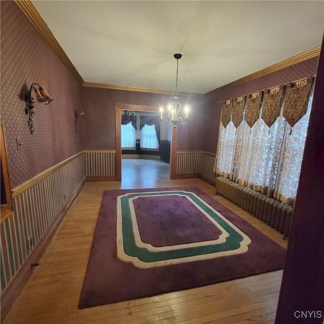 unfurnished dining area with hardwood / wood-style flooring, radiator heating unit, ornamental molding, and an inviting chandelier