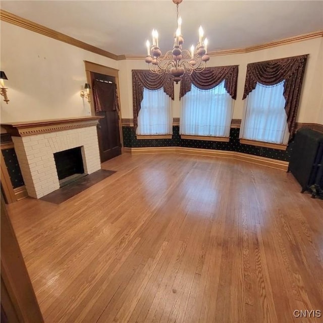 unfurnished living room featuring a fireplace, wood-type flooring, ornamental molding, and a notable chandelier