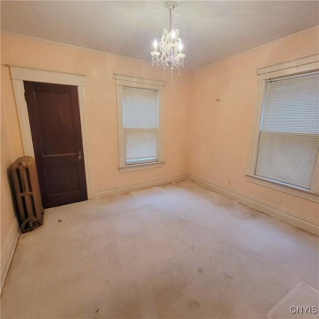 carpeted spare room with radiator and an inviting chandelier