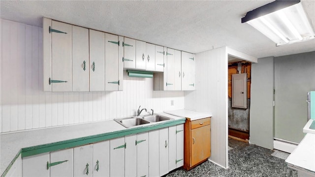 kitchen with electric panel, sink, a textured ceiling, a baseboard radiator, and white cabinetry