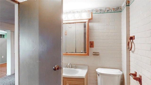 bathroom featuring hardwood / wood-style flooring, vanity, toilet, and brick wall