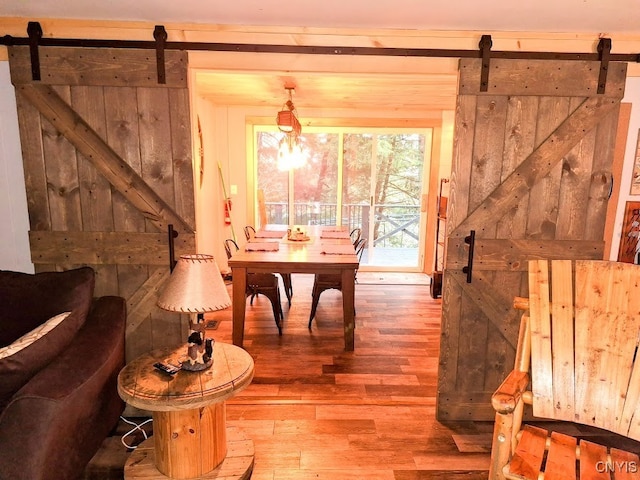 dining area with a barn door, light hardwood / wood-style floors, and a notable chandelier