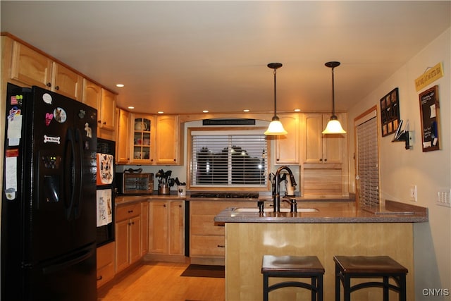 kitchen featuring kitchen peninsula, a kitchen breakfast bar, light wood-type flooring, black refrigerator with ice dispenser, and pendant lighting