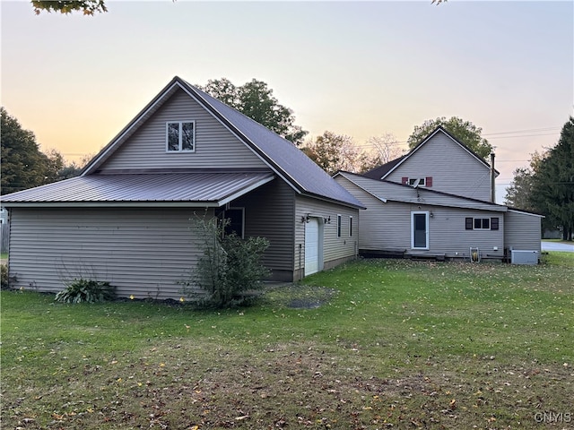 back house at dusk featuring central AC unit, a garage, and a yard