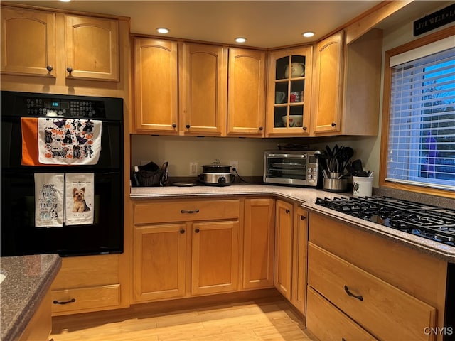 kitchen with double oven, dark stone counters, light hardwood / wood-style floors, and gas stovetop