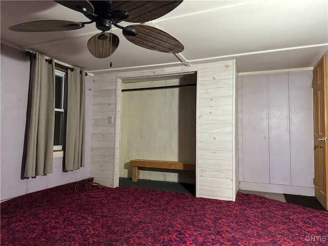 unfurnished bedroom with carpet flooring, ceiling fan, and wood walls