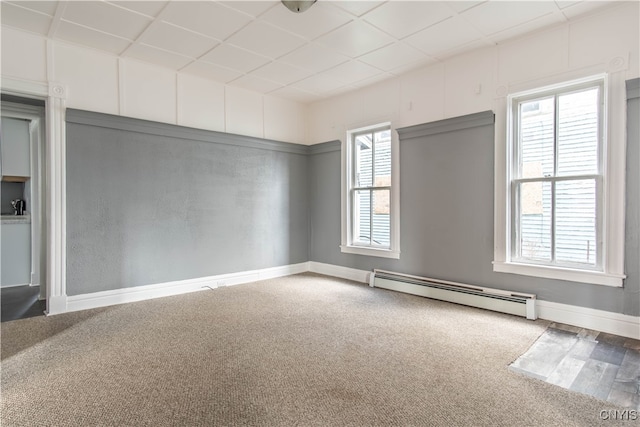 empty room with carpet flooring, a paneled ceiling, and a baseboard heating unit