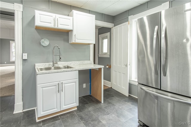 kitchen featuring light stone countertops, white cabinetry, stainless steel refrigerator, and sink