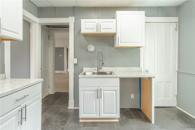 kitchen featuring a paneled ceiling, sink, and white cabinets