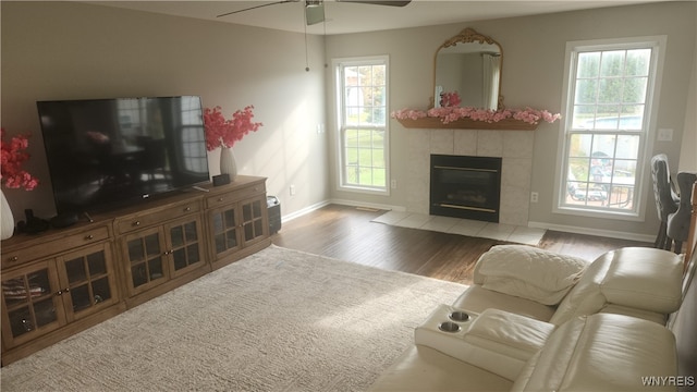 living room with a tiled fireplace, a healthy amount of sunlight, ceiling fan, and wood-type flooring