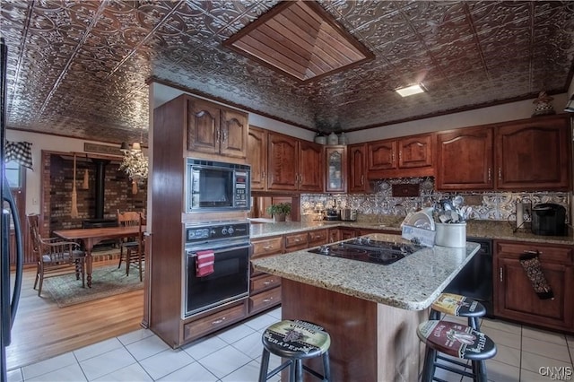 kitchen featuring light stone countertops, a kitchen bar, a kitchen island, black appliances, and light wood-type flooring