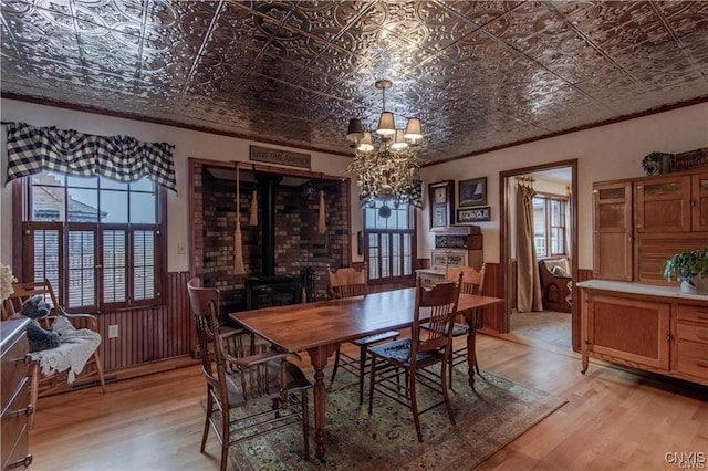 dining area with a chandelier, light wood-type flooring, a wood stove, and crown molding