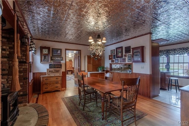 dining area featuring a wood stove, light wood-type flooring, ornamental molding, and an inviting chandelier