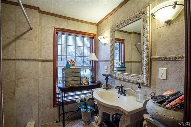 bathroom featuring sink, crown molding, a textured ceiling, tiled shower, and tile walls