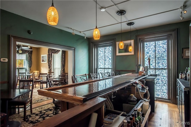 bar featuring rail lighting, a healthy amount of sunlight, and hanging light fixtures