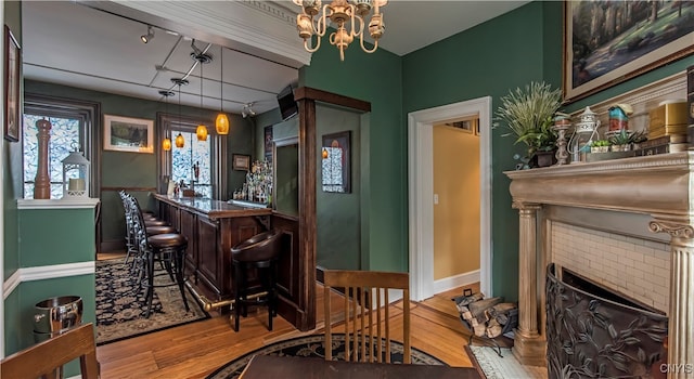 bar featuring hanging light fixtures, a brick fireplace, light hardwood / wood-style flooring, a notable chandelier, and dark brown cabinets