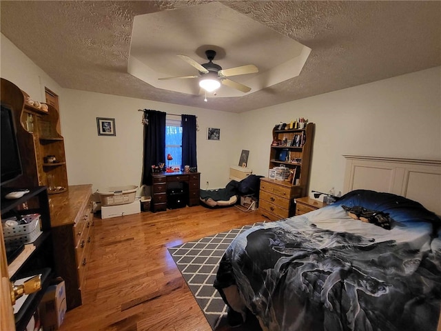 bedroom featuring a tray ceiling, ceiling fan, hardwood / wood-style floors, and a textured ceiling