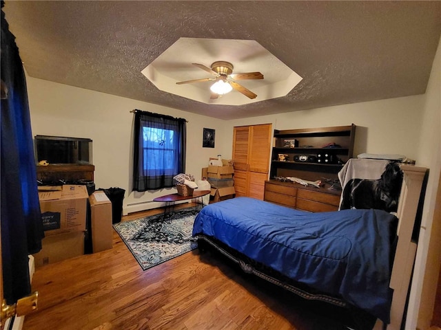 bedroom with a raised ceiling, ceiling fan, a textured ceiling, and hardwood / wood-style flooring