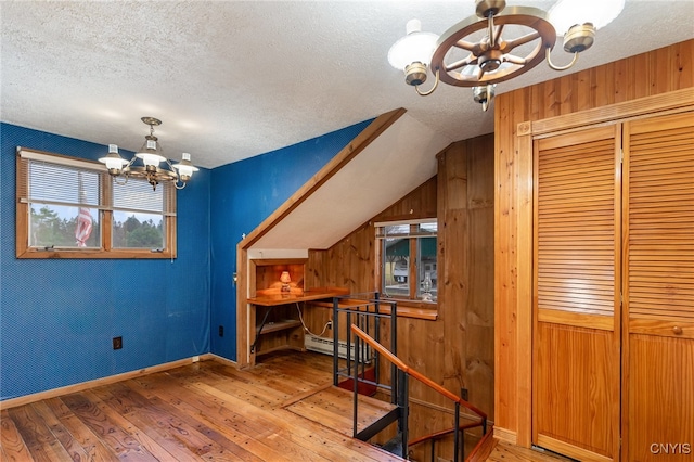 additional living space featuring an inviting chandelier, baseboard heating, hardwood / wood-style floors, a textured ceiling, and lofted ceiling