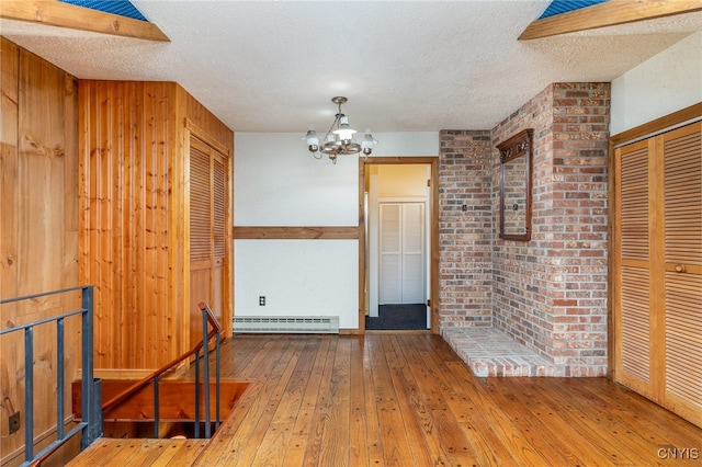 empty room featuring hardwood / wood-style floors, a textured ceiling, wooden walls, and a baseboard radiator