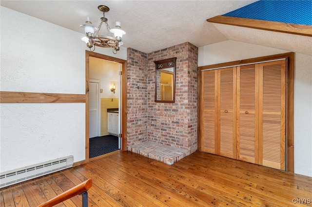 interior space with baseboard heating, hardwood / wood-style floors, a chandelier, a textured ceiling, and lofted ceiling