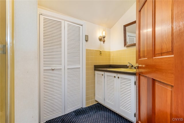 bathroom with vaulted ceiling, vanity, and tile walls