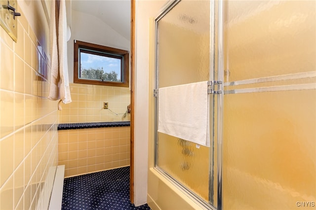 bathroom featuring combined bath / shower with glass door, vaulted ceiling, and tile walls