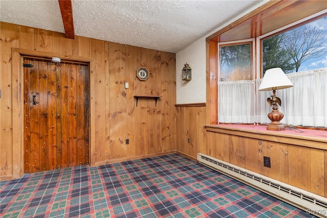 interior space with a textured ceiling, beam ceiling, baseboard heating, and wooden walls