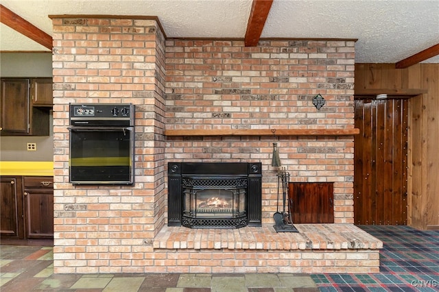 interior space with beam ceiling, a brick fireplace, a textured ceiling, black oven, and wooden walls