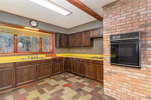 kitchen with a textured ceiling, dark brown cabinetry, sink, beam ceiling, and oven