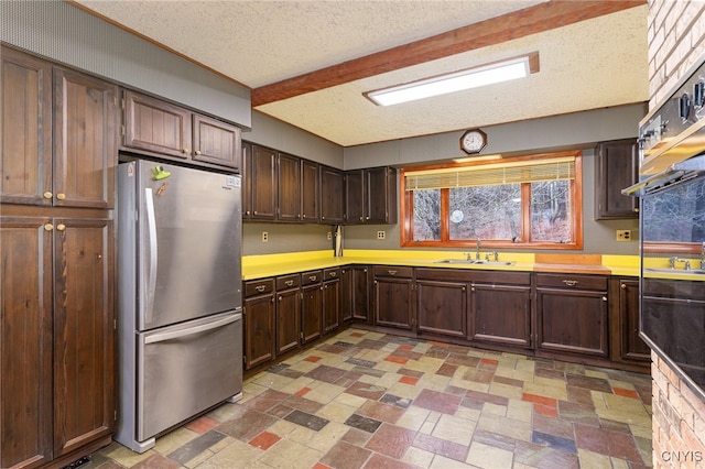 kitchen featuring sink, beamed ceiling, stainless steel fridge, a textured ceiling, and dark brown cabinets