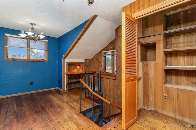 additional living space with hardwood / wood-style flooring, a chandelier, a textured ceiling, and vaulted ceiling