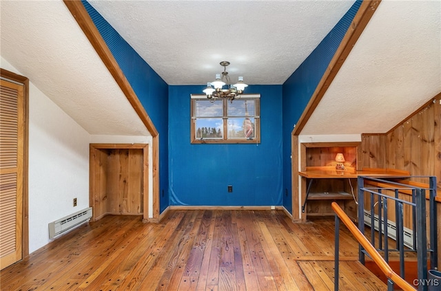 additional living space with dark hardwood / wood-style flooring, a baseboard radiator, a textured ceiling, and a notable chandelier