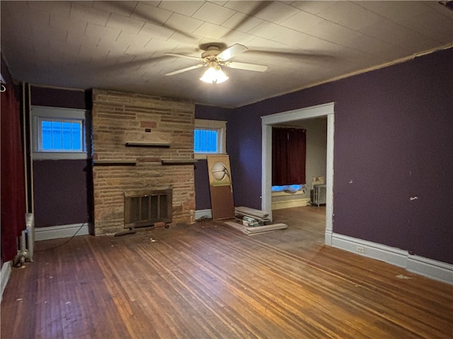 unfurnished living room featuring hardwood / wood-style flooring, ceiling fan, a stone fireplace, and radiator