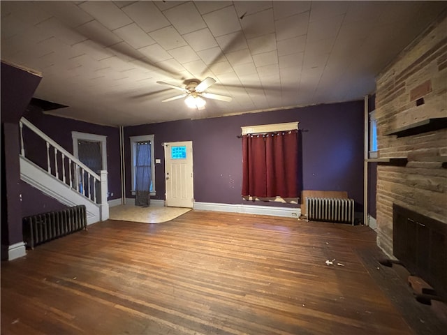 unfurnished living room featuring a stone fireplace, ceiling fan, radiator heating unit, and hardwood / wood-style floors