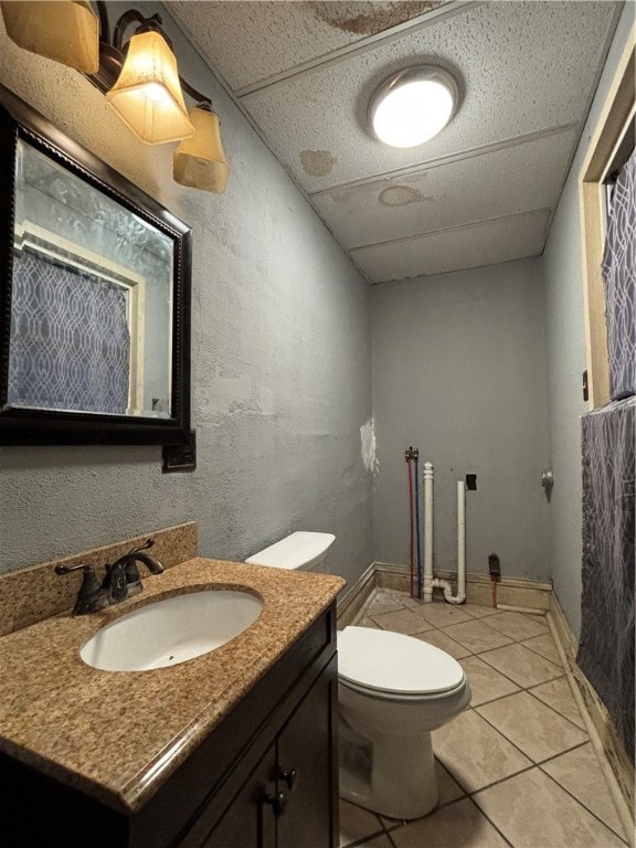 bathroom with tile patterned flooring, vanity, a drop ceiling, and toilet