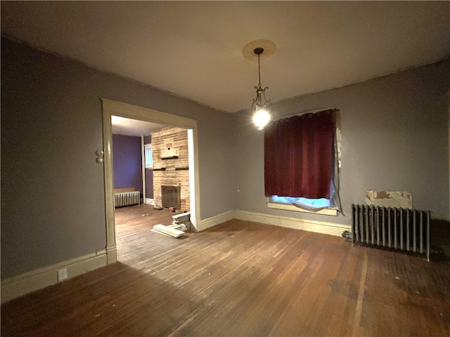 unfurnished dining area featuring hardwood / wood-style flooring, a stone fireplace, and radiator