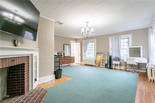 interior space featuring a brick fireplace, radiator, crown molding, wood-type flooring, and an inviting chandelier