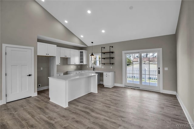 kitchen with a center island, high vaulted ceiling, light hardwood / wood-style flooring, decorative light fixtures, and white cabinetry