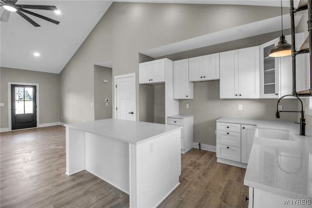 kitchen featuring a center island, high vaulted ceiling, decorative light fixtures, light stone counters, and white cabinetry