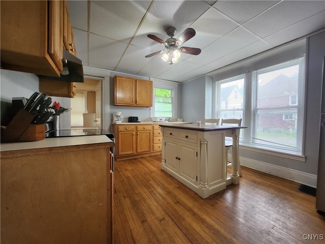 kitchen featuring ceiling fan, a center island, a drop ceiling, and light wood-type flooring