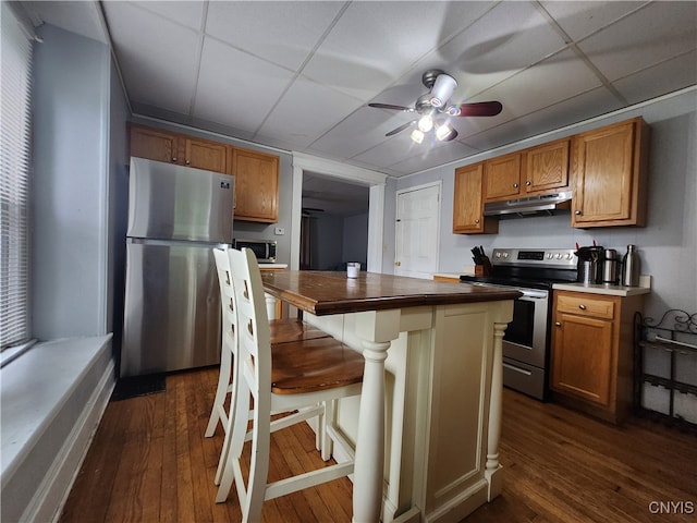 kitchen with a kitchen breakfast bar, dark hardwood / wood-style floors, stainless steel appliances, and ceiling fan